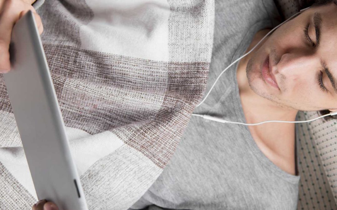 homme allongé avec une tablette et des écouteurs
